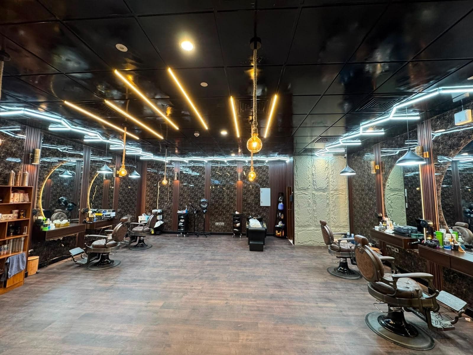 Inside Les Messieurs: four leather barber chairs under amber light bars and a black gloss ceiling