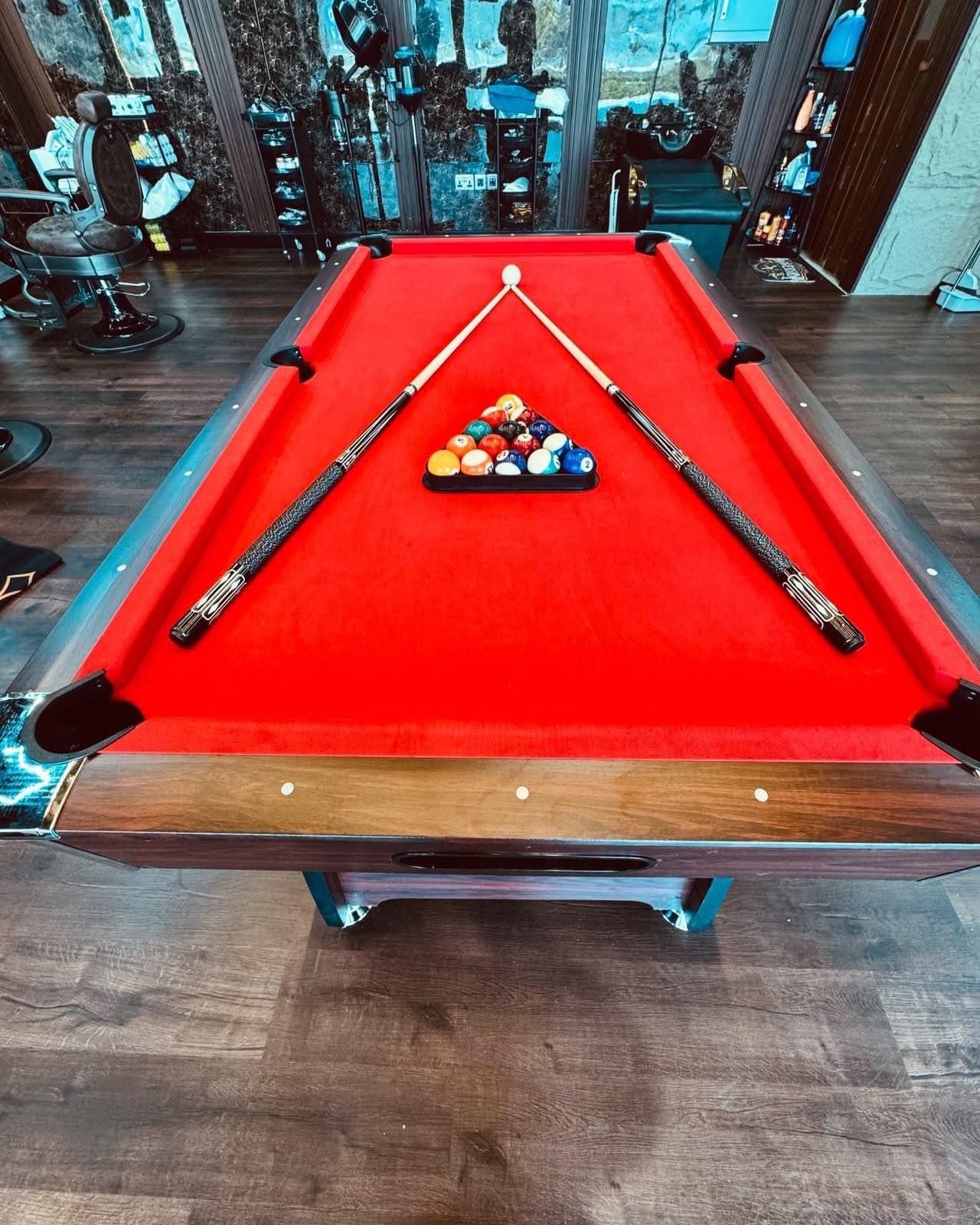 Red pool table, racked, with two cues laid in a triangle